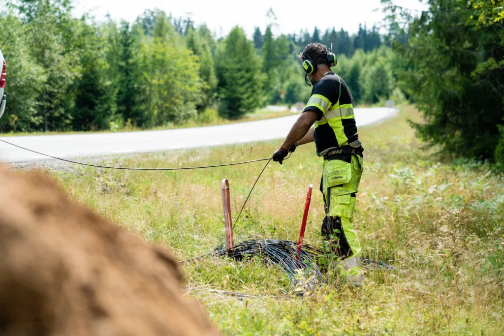 Tekniker som lägger fiberkabel vid vägkant i lantlig miljö.