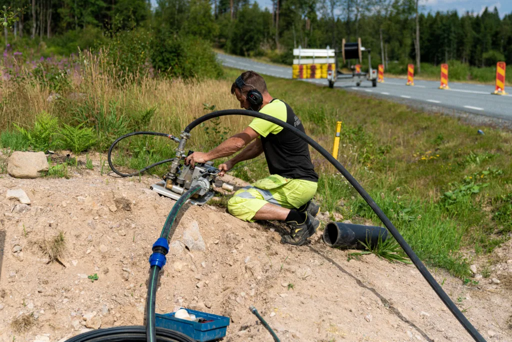Tekniker som lägger fiberkabel vid vägkant i lantlig miljö.